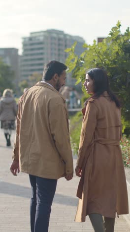 Video-Vertical-De-Una-Amorosa-Pareja-Musulmana-En-Una-Cita-Caminando-Por-El-Parque-De-La-Ciudad-Tomados-De-La-Mano